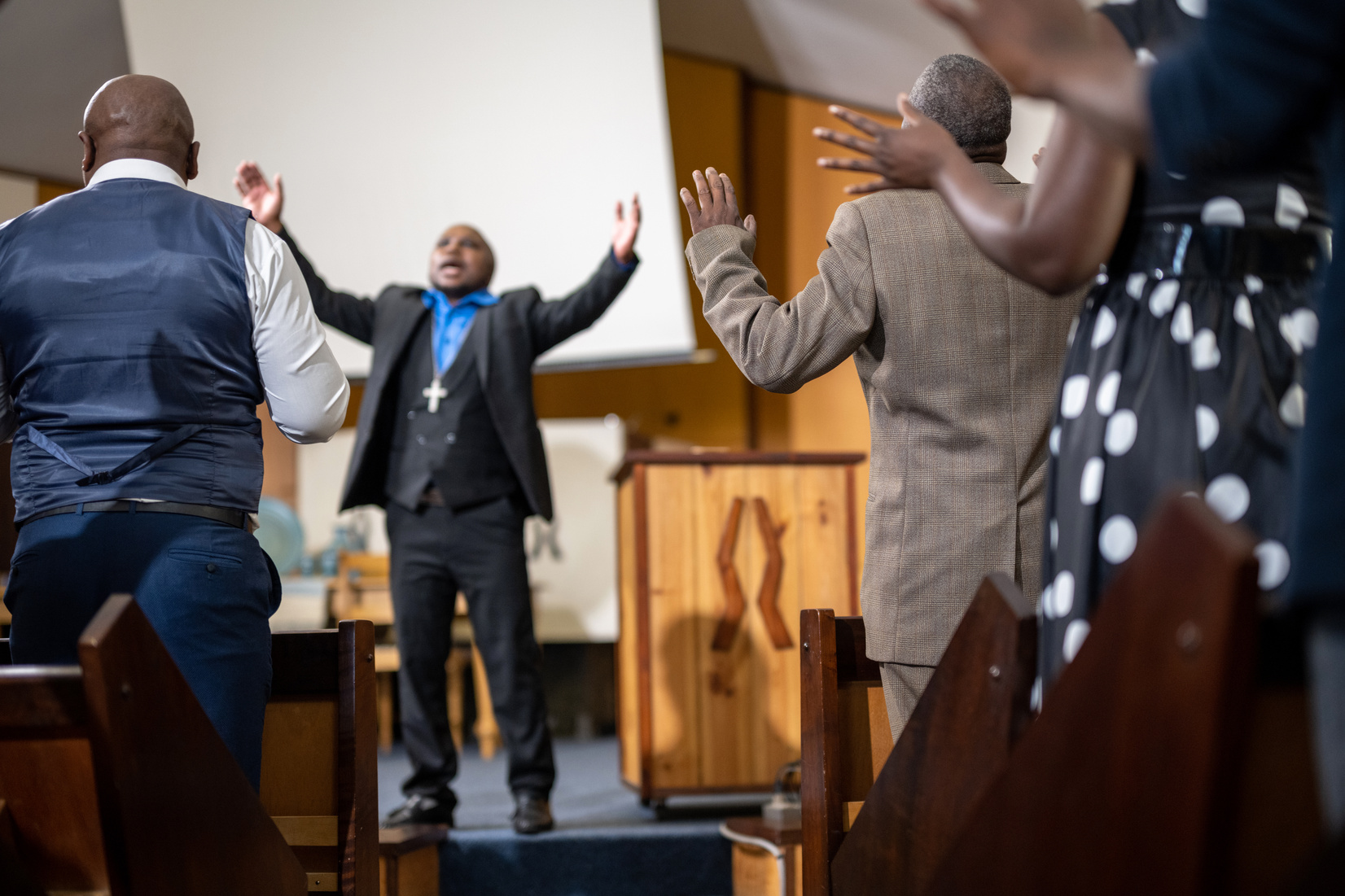 Pastor stand preaching with arms raised in front of congregation
